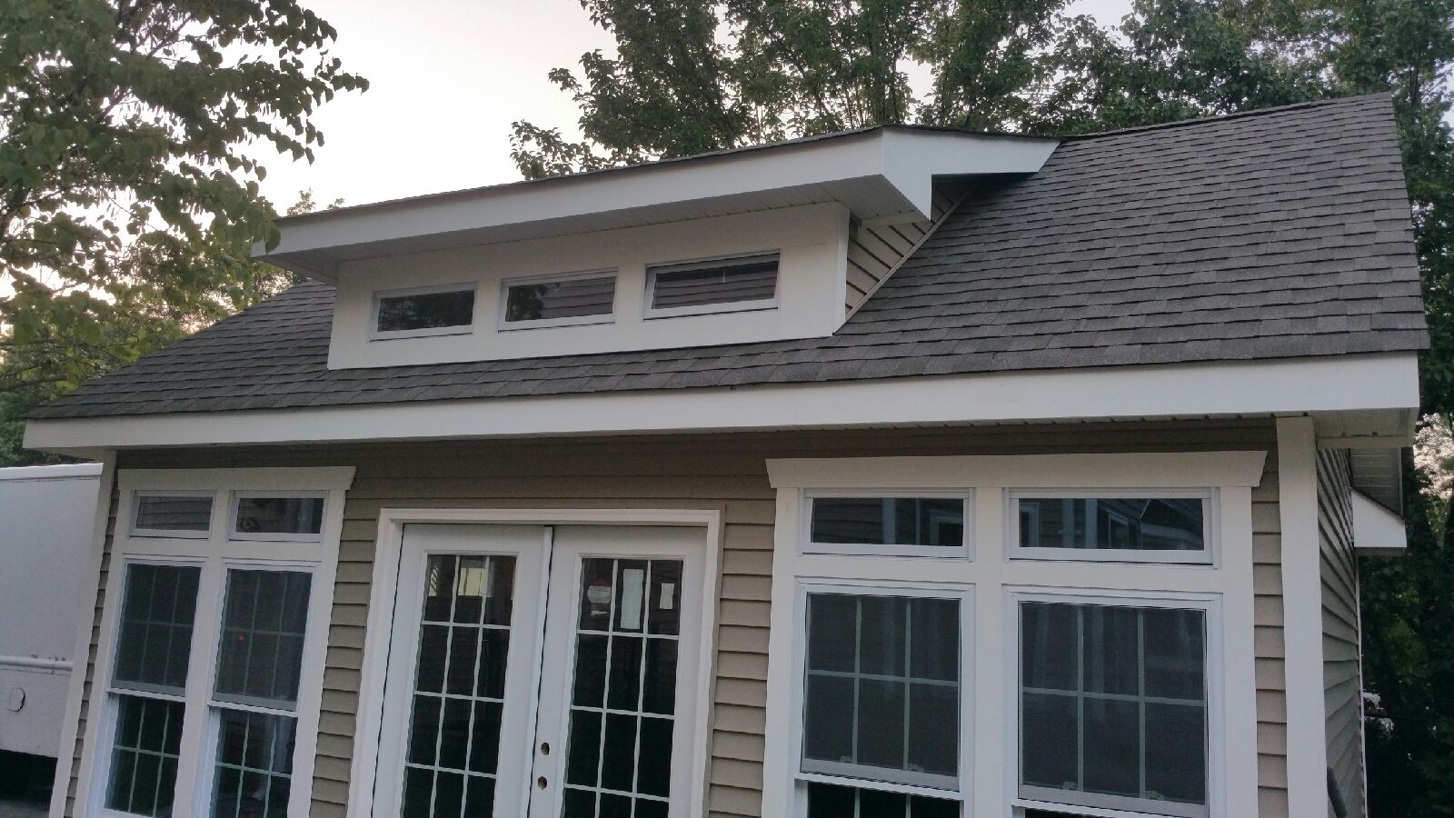 Close-up view of the roofline and upper transom dormer windows on a custom detached garage with tan siding and white trim.