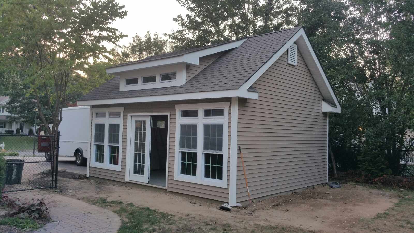 Side view of a custom detached garage featuring large white-trimmed windows, a dormer, and a framed opening for double doors.